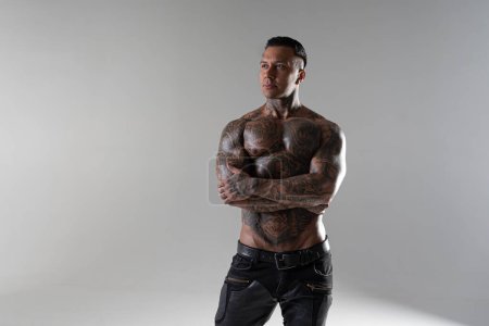 Junge hübsche Bodybuilderin posiert, Athlet zeigt Bodybuilding-Pose. heißer tätowierter Mann mit schönem Körper zeigt seine Muskeln im Studio