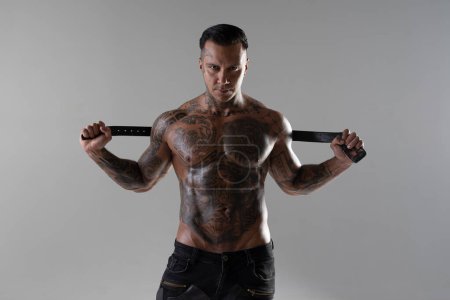 Photo for Muscular shirtless young man with whip in a mask.Brutal handsome man with tattooed body. Men tattoo casual fashion. Portrait of handsome male model. Muscular athletic sexy male with naked torso. - Royalty Free Image
