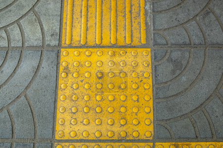 Blocs en braille jaune sur le trottoir, offrant une voie d'accès aux personnes ayant une déficience visuelle.