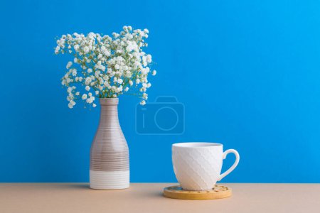 Small white flowers on a blue background. White flowers in a vase. coffe cup