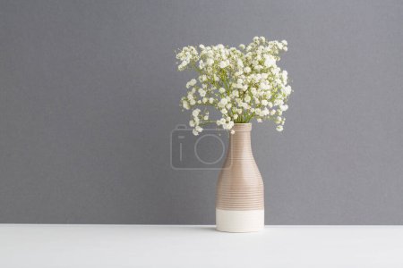 Téléchargez les photos : Petites fleurs blanches sur fond gris. Décor doux pour la maison. Fleurs blanches dans un vase. - en image libre de droit