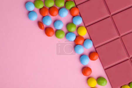 Téléchargez les photos : Barre de chocolat rubis avec des comprimés de bonbons au chocolat colorés sur fond rose - en image libre de droit