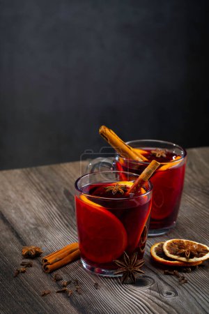 Foto de Copa de vino caliente con rodajas de naranja. Vino caliente e ingredientes en una mesa de madera. Disparos de mano - Imagen libre de derechos