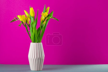 Foto de Tulipanes amarillos en jarrón sobre la mesa sobre fondo magenta - Imagen libre de derechos