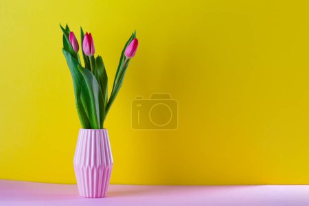 Foto de Ramo de tulipanes rosados en un jarrón sobre un fondo amarillo - Imagen libre de derechos