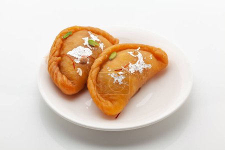 Téléchargez les photos : Deux morceaux de Gujiya doux traditionnel indien sur une assiette blanche. Le sucré est fait de maïs (farine), et de ghee, rempli de fruits secs. Vue de dessus, isolé sur blanc. - en image libre de droit