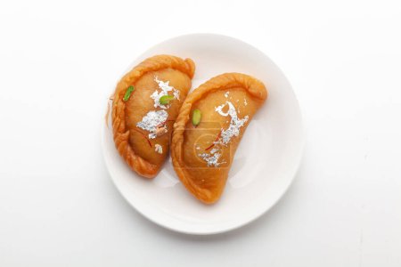 Téléchargez les photos : Deux morceaux de Gujiya doux traditionnel indien sur une assiette blanche. Le sucré est fait de maïs (farine), et de ghee, rempli de fruits secs. Vue de face, isolé sur blanc. - en image libre de droit