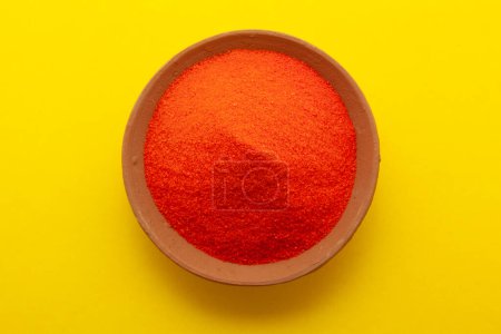 Draufsicht der orangefarbenen Farbe traditionelles Rangoli-Pulver in Tonlampe isoliert auf gelbem Hintergrund.