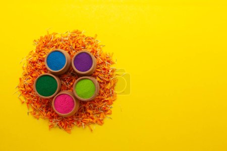 Top view of colorful traditional Rangoli powder in clay pots, on orange marigold petals.