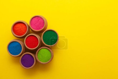 Top view of colorful traditional Rangoli powder in clay pots isolated on a yellow background.