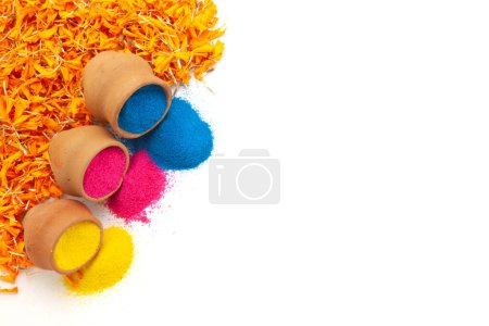 Clay pots filled with various colors of Holi powder spilled out, placed on marigold leaves. Isolated on a white background.