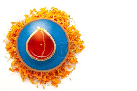 Un Diwali diya (une lampe à huile de terre) est vu d'une vue de dessus, placé sur des pétales de souci orange, isolé sur un fond blanc.