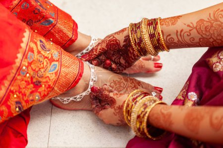 Konzept der indischen Hochzeitszeremonie. Eine indische Braut bekommt ihre silbernen Fußkettchen von einer anderen Frau angezogen.