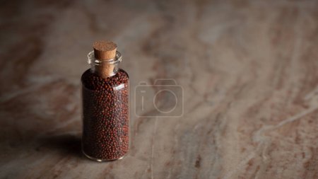 A small glass bottle filled with organic Ragi (Eleusine coracana) or finger millet is placed on a marble background.