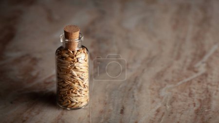 Una pequeña botella de vidrio llena de cebada orgánica (Hordeum Vulgare) o granos de jau se coloca sobre un fondo de mármol.