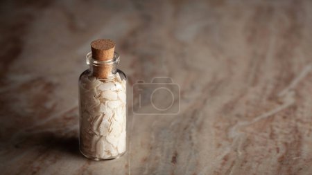 Una pequeña botella de vidrio llena de arroz orgánico Flattened (Oryza Sativa) o Poha se coloca sobre un fondo de mármol.