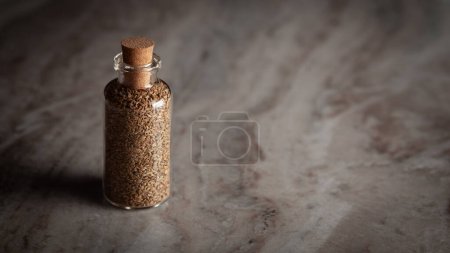 Eine kleine Glasflasche gefüllt mit Bio-Karamellsamen (Trachyspermum ammi) oder Ajwain steht auf einem Marmorgrund.