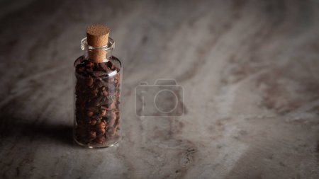 Une petite bouteille en verre remplie de girofle biologique (Syzygium aromaticum) ou indienne longue est placée sur un fond de marbre.