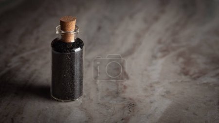 Una pequeña botella de vidrio llena de comino negro orgánico (Nigella sativa) o kalonji se coloca sobre un fondo de mármol.