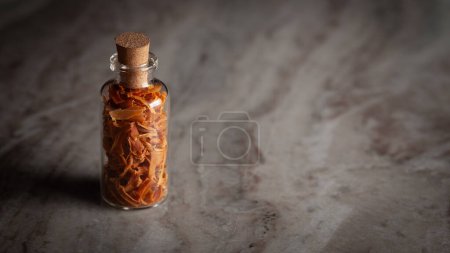 Eine kleine Glasflasche gefüllt mit organischer Muskatblüte (Myristica fragrans) oder Javitri steht auf einem Marmorhintergrund.