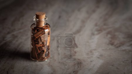 Una pequeña botella de vidrio llena de canela orgánica (Cinnamomum verum) o dalchini se coloca sobre un fondo de mármol.