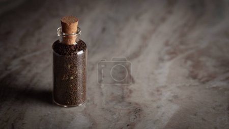 A small glass bottle filled with dry tea leaves. Placed on a marble background.