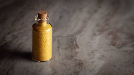 Eine kleine Glasflasche gefüllt mit organischem Heeng (Asafoetida) steht auf einem Marmorhintergrund.