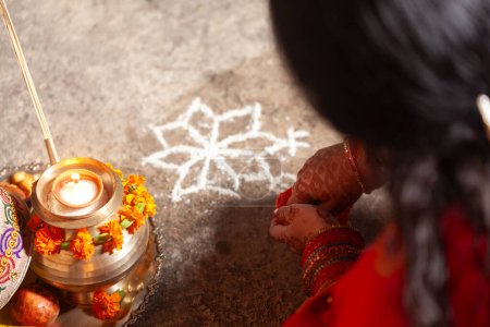 Téléchargez les photos : Une Indienne réalise un motif hindou (rangoli) avantageux pour Karwa Chauth dans un saree rouge. - en image libre de droit