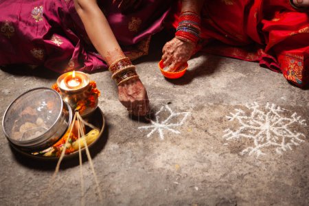 Dos mujeres indias están haciendo un patrón de diseño hindú auspicioso (rangoli) para el Festival Karwa Chauth.