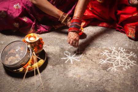 Dos mujeres indias están haciendo un patrón de diseño hindú auspicioso (rangoli) para el Festival Karwa Chauth.