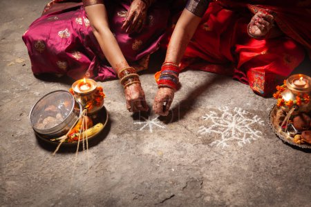 Two Indian women are making an Auspicious Hindu design pattern (rangoli) for the Karwa Chauth Festival.
