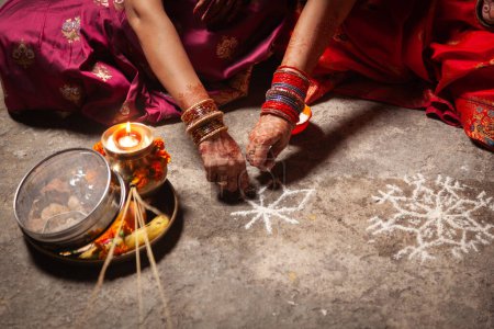 Two Indian women are making an Auspicious Hindu design pattern (rangoli) for the Karwa Chauth Festival.