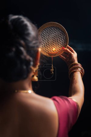 Una mujer india mirando a la luna a través de un tamiz durante el festival Karwa Chauth.