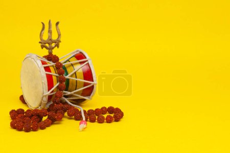 Lord Shivas Damaru or a two-headed Drum musical instrument, Trident or Trishul with Rudraksha bead necklace (Mala). Isolated on a yellow background.