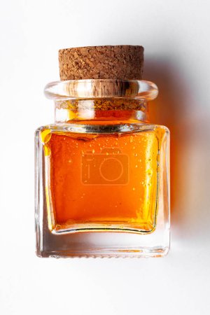 Top-down view of a square glass bottle containing orange color essential oil for cosmetics and natural medicine.