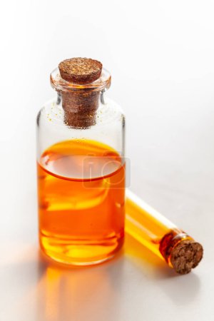 A round glass bottle and a vial containing orange color essential oil for cosmetics and natural medicine.