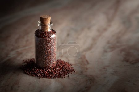 Eine kleine Glasflasche gefüllt mit organischem Ragi (Eleusine coracana) oder Fingerhirse wird auf einem Marmorhintergrund platziert.