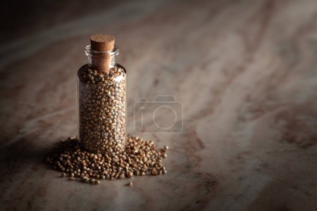 Eine kleine Glasflasche gefüllt mit organischer Perlhirse (Pennisetum glaucum) oder Bajra steht auf einem Marmorhintergrund..