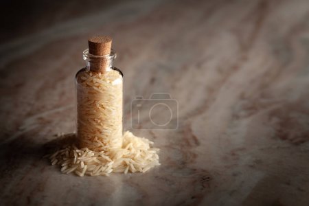 Eine kleine Glasflasche mit weißem Bio-Reis (Oryza sativa) steht auf einem Marmorhintergrund.