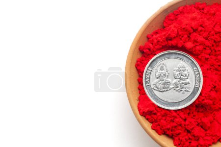 Blick von oben auf einen irdenen Topf, gefüllt mit rotfarbenem Waschbecken. Eine Silbermünze mit eingravierten Hindu-Gottheiten Ganesha und Laxmi. Isoliert auf weißem Hintergrund.