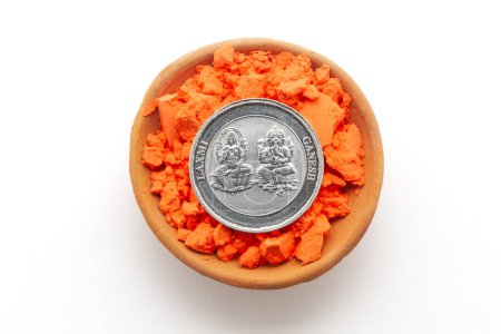 Blick von oben auf einen irdenen Topf, gefüllt mit orangefarbenem Waschbecken. Eine Silbermünze mit eingravierten Hindu-Gottheiten Ganesha und Laxmi. Isoliert auf weißem Hintergrund.