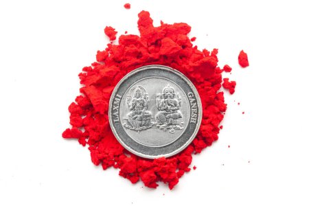 Ansicht einer Silbermünze mit eingravierten Hindu-Gottheiten "Ganesha und Laxmi" von oben über einer rot gefärbten Sindoor (Zinnober) isoliert auf weißem Hintergrund.