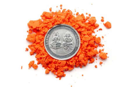 Vista de arriba hacia abajo de una moneda de plata grabada con deidades hindúes "Ganesha y Laxmi" se coloca sobre un sindoor (bermellón) de color naranja aislado sobre un fondo blanco.