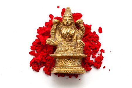 The brass idol of the Hindu Goddess Lakshmi is placed over a red-colored sindoor (vermilion) isolated on a white background. Top view