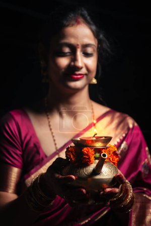 A traditional Indian woman holds a decorated brass Karwa with closed eyes for Karwa Chauth, an Indian tradition.