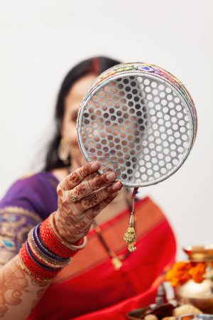 Una mujer india alegre celebra Karwa Chauth, un festival hindú, vistiendo un saree tradicional y colorido y mirando a través de un tamiz.