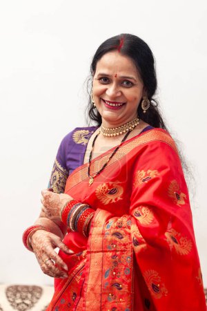 A beautiful, happy Indian woman is wearing a red saree and looking directly at the camera.