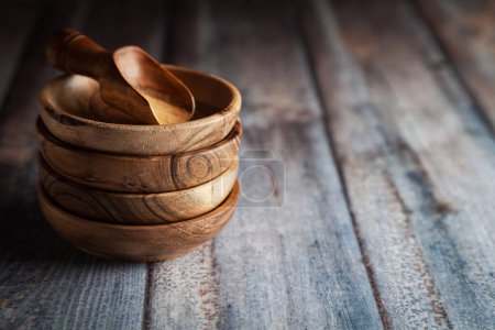 Stacked Wooden bowls, along with a wooden scoop on a wooden background.