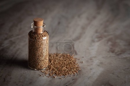 Foto de Una pequeña botella de vidrio llena de semillas de Carambola orgánica (Trachyspermum ammi) o Ajwain se coloca sobre un fondo de mármol. - Imagen libre de derechos