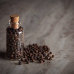 A small glass bottle filled with organic Black pepper (Piper nigrum) is placed on a marble background.